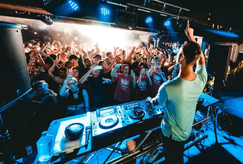 DJ with his hand up in front of a cheerful crowd